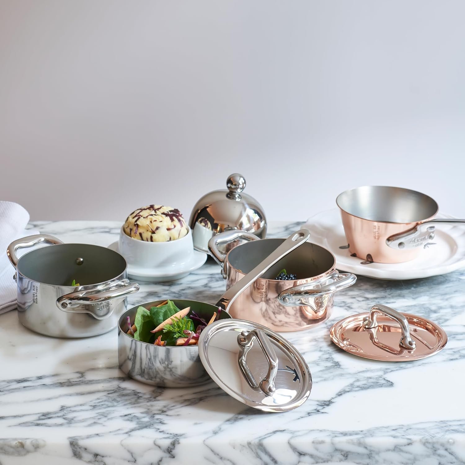 Juegos de ollas Mauviel de bronce y acero de lujo sobre meson de marmol